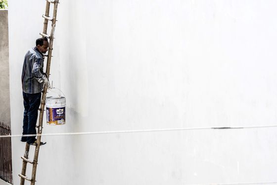 Peintre à l'échelle appliquant une finition sur un grand mur clair